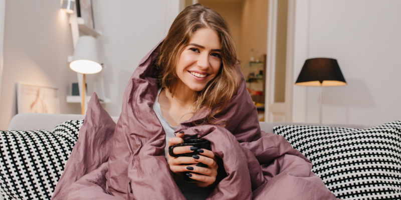 Mevrouw zit met een kopje thee op de bank en heeft het koud