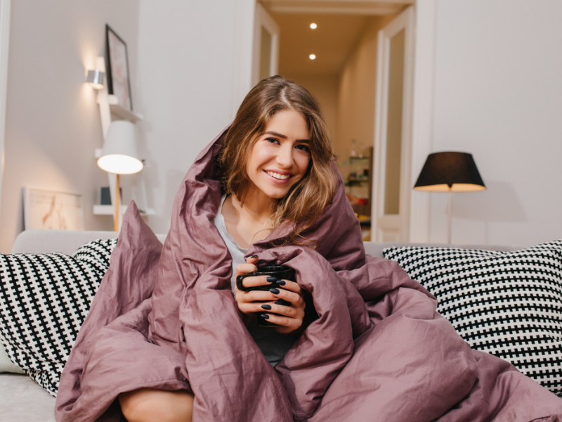 Mevrouw zit met een kopje thee op de bank en heeft het koud