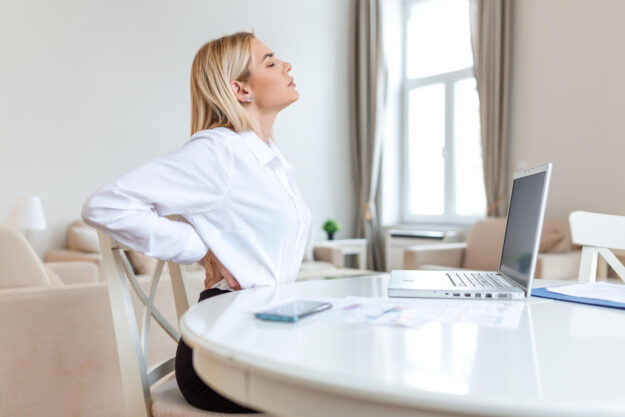 Vrouw met chronische rugklachten ziet op een stoel achter een laptop.
