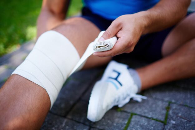 Man bindt zijn knie in met drukverband. Leeftijd beïnvloed blessures